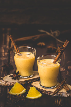 Two glasses of eggnog with cinnamon sticks on dark wooden background. Auld Man's milk, Coquito or Creme de Vie or Eggnog. Vertical with copy space.の写真素材