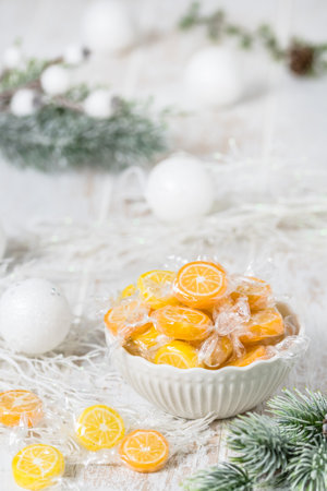 Bowl with candies in the form of orange and lemon slices, individually wrapped in foil, on white background with christmas decoration, verticalの写真素材