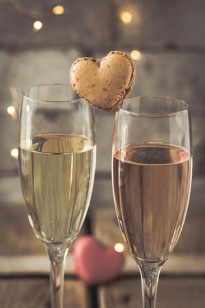Two glasses with sparkling wine and heart shaped macarons on a rustic wooden table, romantic atmosphere, verticalの写真素材
