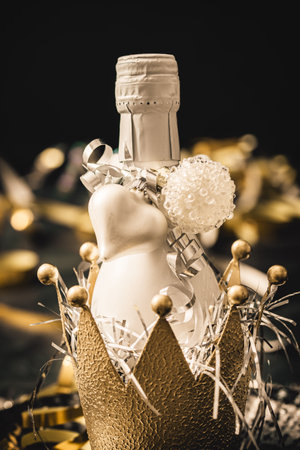 Small white bottle with sparkling wine in a decorative golden metal crown, decorated by a white heart. Vertical close-up.の写真素材