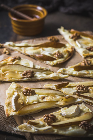 Pieces of a tarte flambee witgh pear, goat cheese, honey and walnuts on dark rustic wooden background, verticalの写真素材
