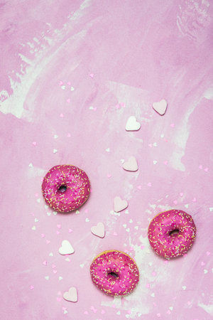 Donuts, Berliner, Krapfen with pink sugar icing on pink textured background, decorated with pink and white sugar and paper hearts, top view with copy spaceの写真素材
