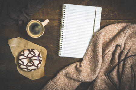 Donut, coffee and a notebook on a dark wooden table, cozy scene of a coffee break, top view with copy spaceの写真素材