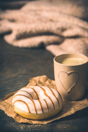 Donut on a dark wooden table, coffee mug with a heart and a wool sweater on the background, cozy atmosphere, coffee break, verticalの写真素材