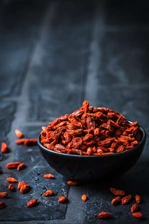 Bowl with dried Goji berries, chinese wolfberries, on black background, vertical with copy spaceの写真素材