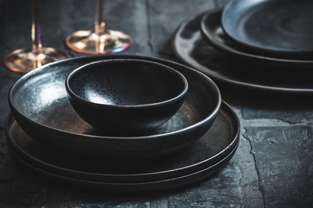 Black stoneware plates and bowls on a rustic black tableの写真素材