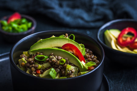 Lentil salad with avocado and red pepper in a black bowl on black background. Vegetarian and vegan foods.の写真素材
