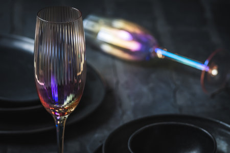Pink shimmering champagne glass and black stoneware on a rustic black table, one glass lying in the backgroundの写真素材