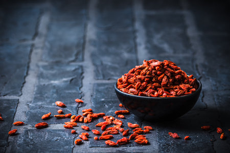 Bowl with dried Goji berries, chinese wolfberries, on black background, vertical with copy spaceの写真素材