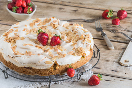 Whole rhubarb pie with meringue topping, roasted almonds and fresh strawberries on a cooling rack on an old rustic wooden tableの写真素材