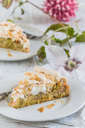 Pieces of rhubarb pie with meringue topping and roasted almonds on white wooden background, verticalの写真素材