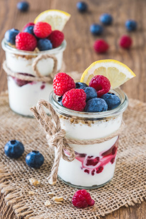 Yogurt with berries and cereals in a glass on a rustic wooden table, verticalの写真素材