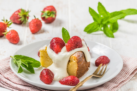 Piece of homemade cheesecake with whipped cream and fresh strawberries on white wooden background, decorated with fresh mint leavesの写真素材