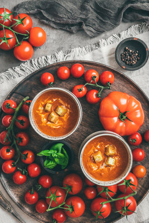 Two cups of homemade tomato soup on a wooden plate with a variety of ripe tomatoes, vertical, top viewの写真素材
