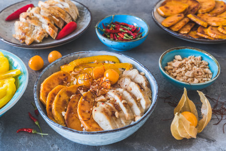 Buddha bowls with spicy chicken, rice, bell pepper, sweet potato and minced peanuts, trend and healthy food, top view on gray backgroundの写真素材