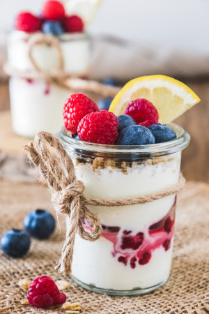 Yogurt with berries and cereals in a glass on a rustic wooden table, verticalの写真素材