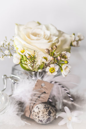 White rose and spring flowers in mason jar decorated with feathers and quail egg, verticalの写真素材