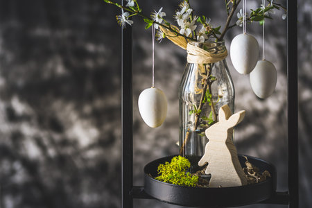 Easter decoration with white cherry blossom branches and white eggs on a black metal stand, gray background, copy spaceの写真素材