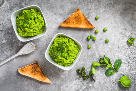 Two bowls of pea puree with basil, mint and roasted bread on rustic gray background, top viewの写真素材