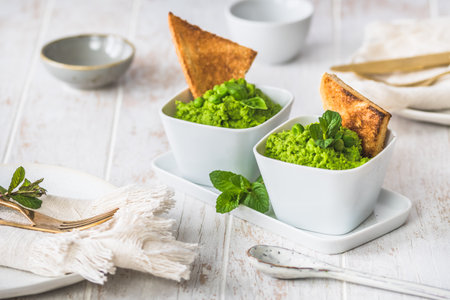 Two bowls of pea puree with basil, mint and roasted bread on white wooden backgroundの写真素材