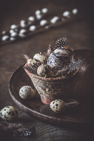 Easter decoration: rustic flower pot with natural quail eggs and feathers on a dark wooden plate and table, verticalの写真素材