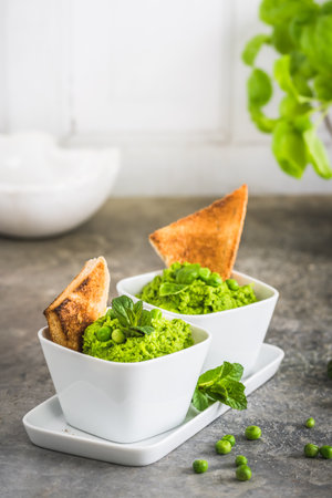 Two bowls of pea puree with basil, mint and roasted bread on rustic gray background, verticalの写真素材