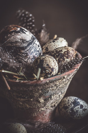 Easter decoration: rustic flower pot with natural quail eggs and feathers on a dark wooden plate and table, vertical with copy spaceの写真素材