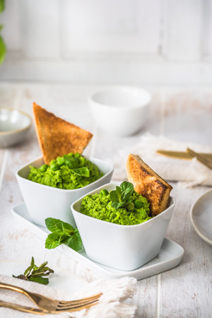 Two bowls of pea puree with basil, mint and roasted bread on white wooden background, vertical, copy spaceの写真素材