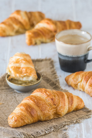 Delicious French croissant on a white wooden table, a cup of coffee and croissants in the background, breakfast scene, verticalの写真素材