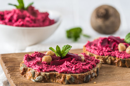 Wooden board of bread slices with beetroot hummus on a white wooden background