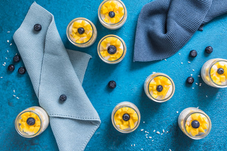 Coconut rice pudding with mango in dessert glasses on blue background, verticalの写真素材