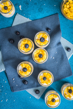 Coconut rice pudding with mango in dessert glasses on blue background, verticalの写真素材