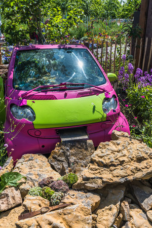 Old pink and green planted car used as a decoration and flower pot in a garden. A watercourse is installed in front. vertical.の写真素材