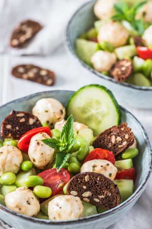 Summer salad with cucumber, mini tomatoes, mini mozzarella and soybeans on white wooden background, verticalの写真素材