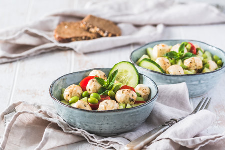 Summer salad with cucumber, mini tomatoes, mini mozzarella and soybeans on white wooden backgroundの写真素材