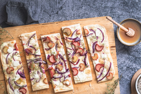 Baked tarte flambee with rhubarb, red onions, goat cheese and honey, cut into strips, gray background, top viewの写真素材