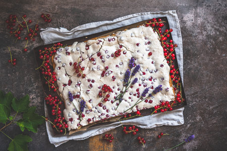 Whole currant cake with crispy meringue on top and fresh fruits as decoration, dark background, top viewの写真素材
