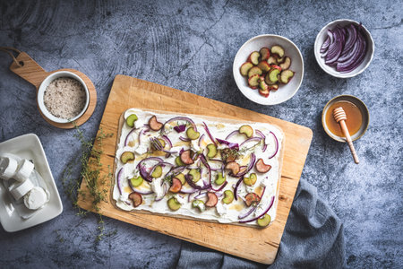 Tarte flambee with rhubarb, red onions, goat cheese and honey, prepared for baking, gray background, top viewの写真素材