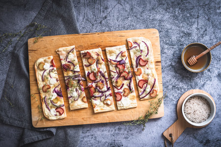 Baked tarte flambee with rhubarb, red onions, goat cheese and honey, cut into strips, gray background, top viewの写真素材