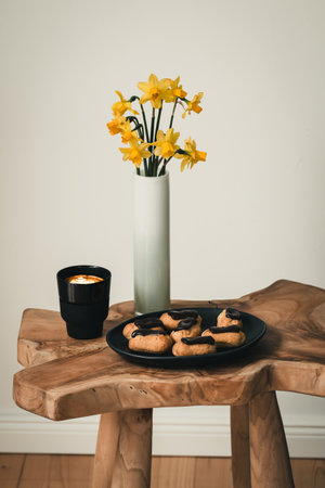 Coffee table with cappuccino, mini brioche with chocolate and a vase with daffodils, concept of modern living, vertical with copy spaceの写真素材