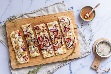 Baked tarte flambee with rhubarb, red onions, goat cheese and honey, cut into strips, marble background, top viewの写真素材