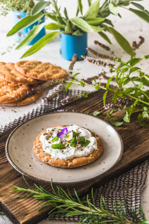 Round crispbread with herbal cream cheese and fresh herbs on a wooden board, verticalの写真素材