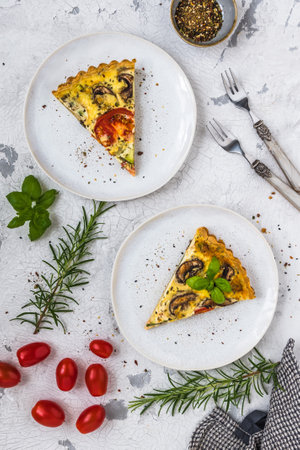 Two pieces of homemade vegetable tart with mushrooms, tomatoes and zucchini on white background, decorated with herbs, top viewの写真素材