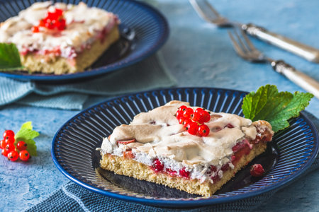Piece of homemade currant cake with crispy meringue on top on a blue plate on blue backgroundの写真素材