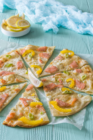 Tarte flambee with salmon, yellow pepper and spring onions on light blue background, verticalの写真素材