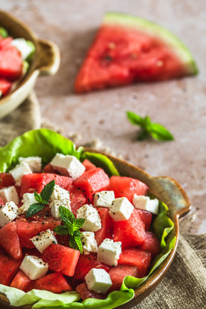 Fresh watermelon salad with feta cheese and mint on beige textured background, decorated with a sprig of mint, verticalの写真素材