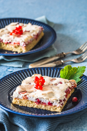 Piece of homemade currant cake with crispy meringue on top on a blue plate on blue backgroundの写真素材