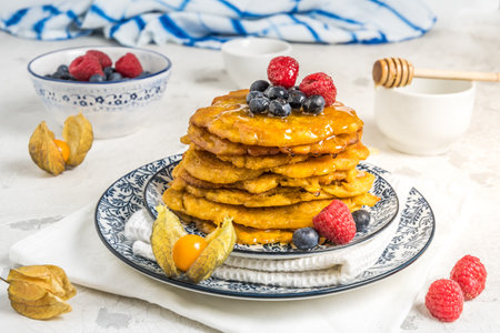 Pile of vegan pancakes with berries and syrup on a blue-white patterned plate on white backgroundの写真素材