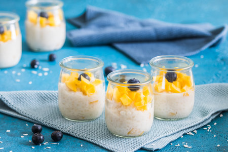 Coconut rice pudding with mango in dessert glasses on blue backgroundの写真素材