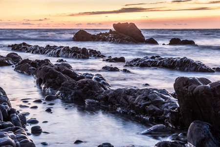 Rocky shore of a coast in the sunset, blurred water from long time exposureの写真素材